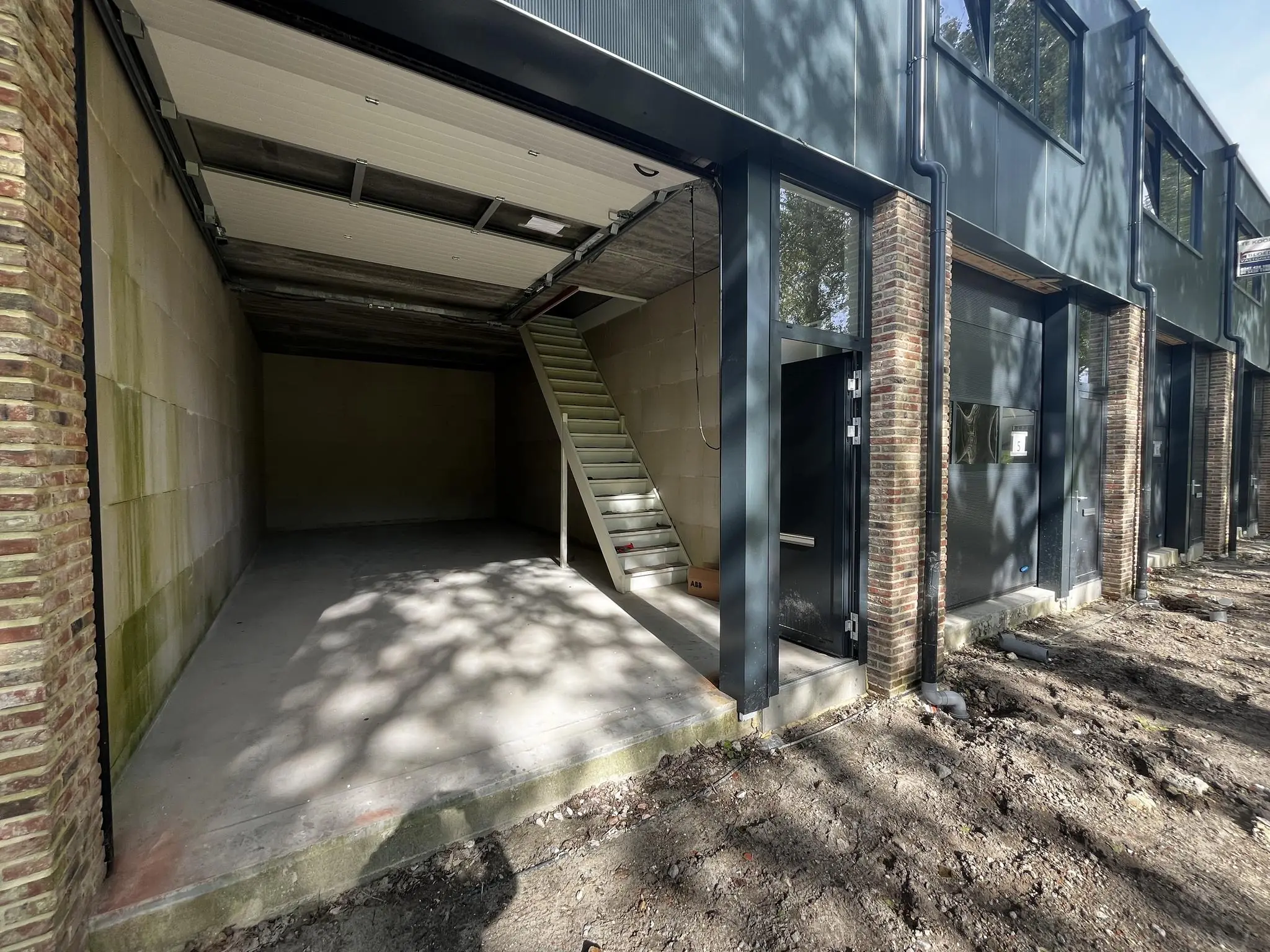 Open garagebox aan Broekdijk-West 19-4 met een betonnen vloer en een trap naar boven.